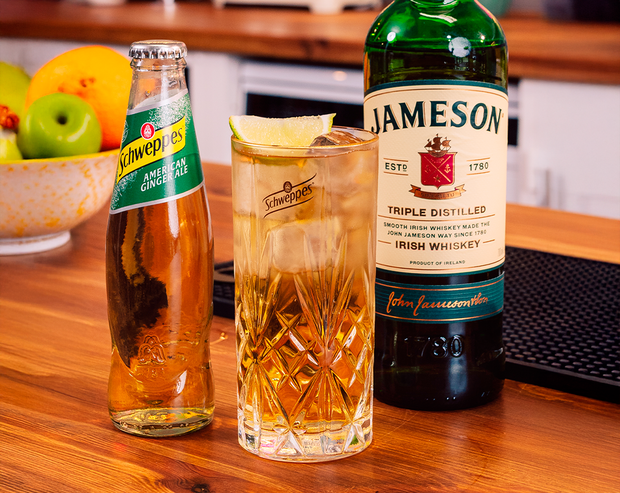 Eine Flasche Schweppes Ginger Ale auf einem Holztisch neben einem Glas und Whiskey.