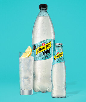 Schweppes Original Bitter Lemon Classic und Zero – Glasflasche neben 1,25-l Flasche, beide mit Kondensperlen auf blauem Hintergrund.